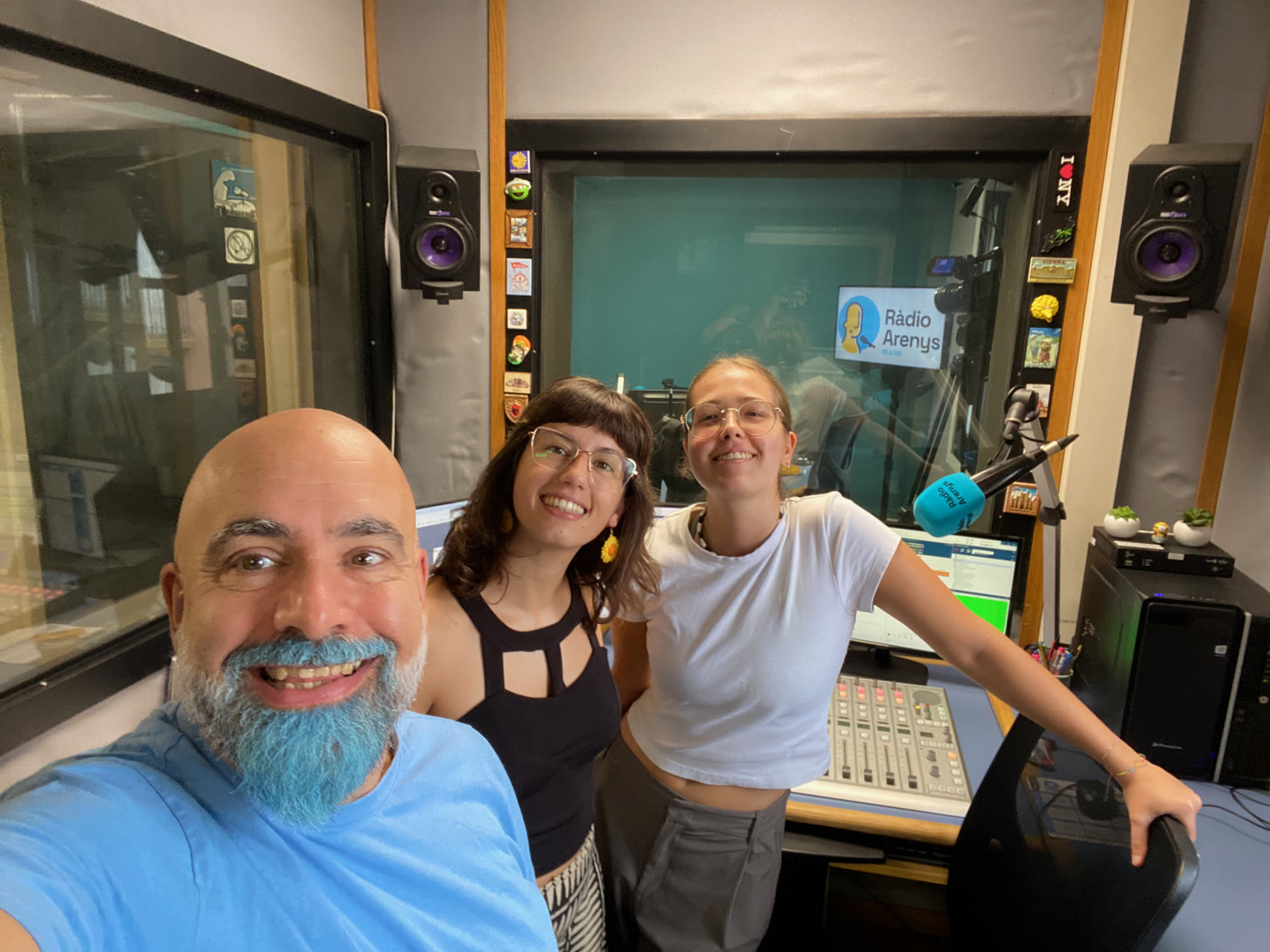 Selfie de David Herrero amb dues companyes a l'estudi 1 de Ràdio Arenys, amb el micròfon blau i el rètol de l'emissora al fons